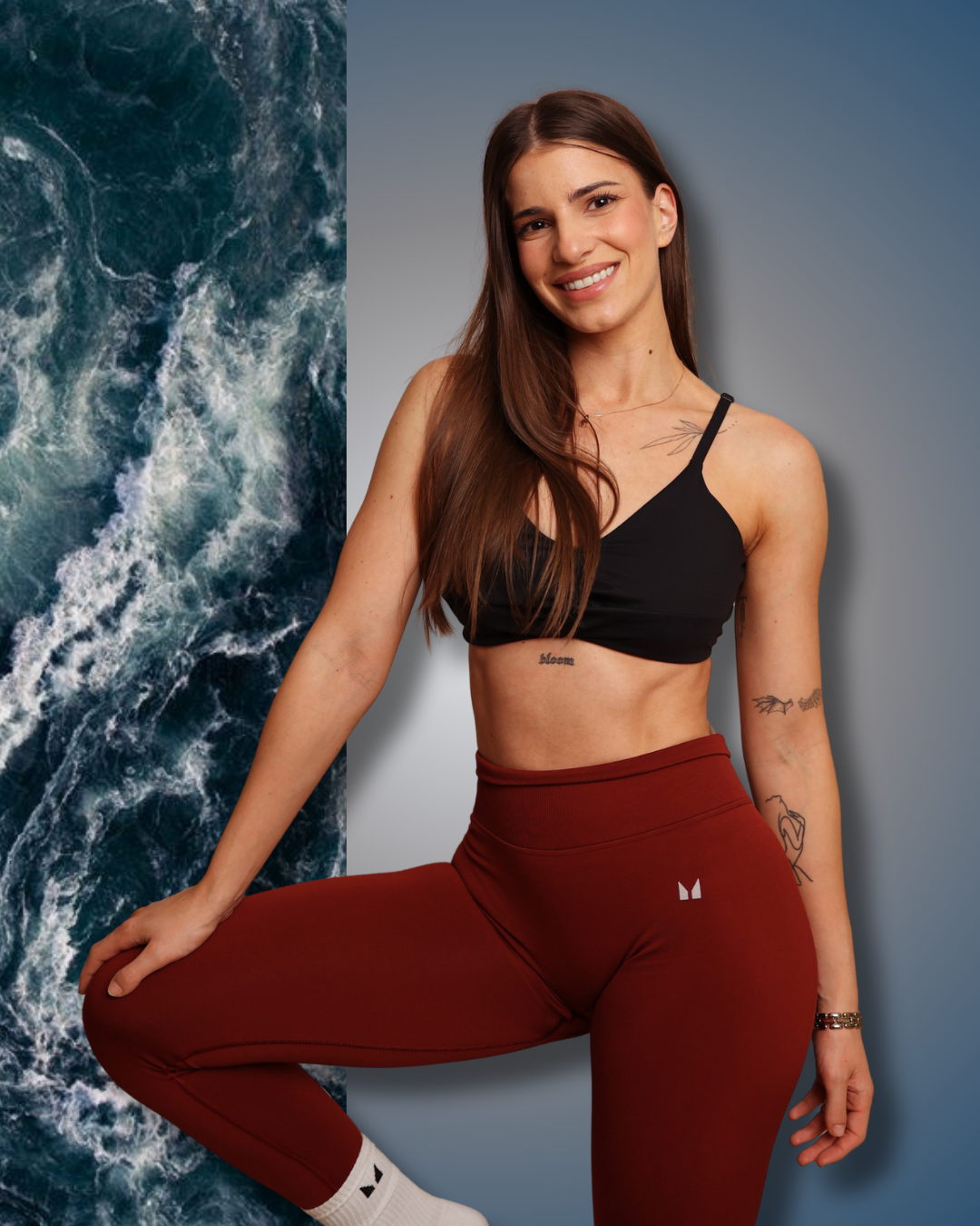 Woman in black sports bra and red leggings posing against a gray background with ocean waves on the left.